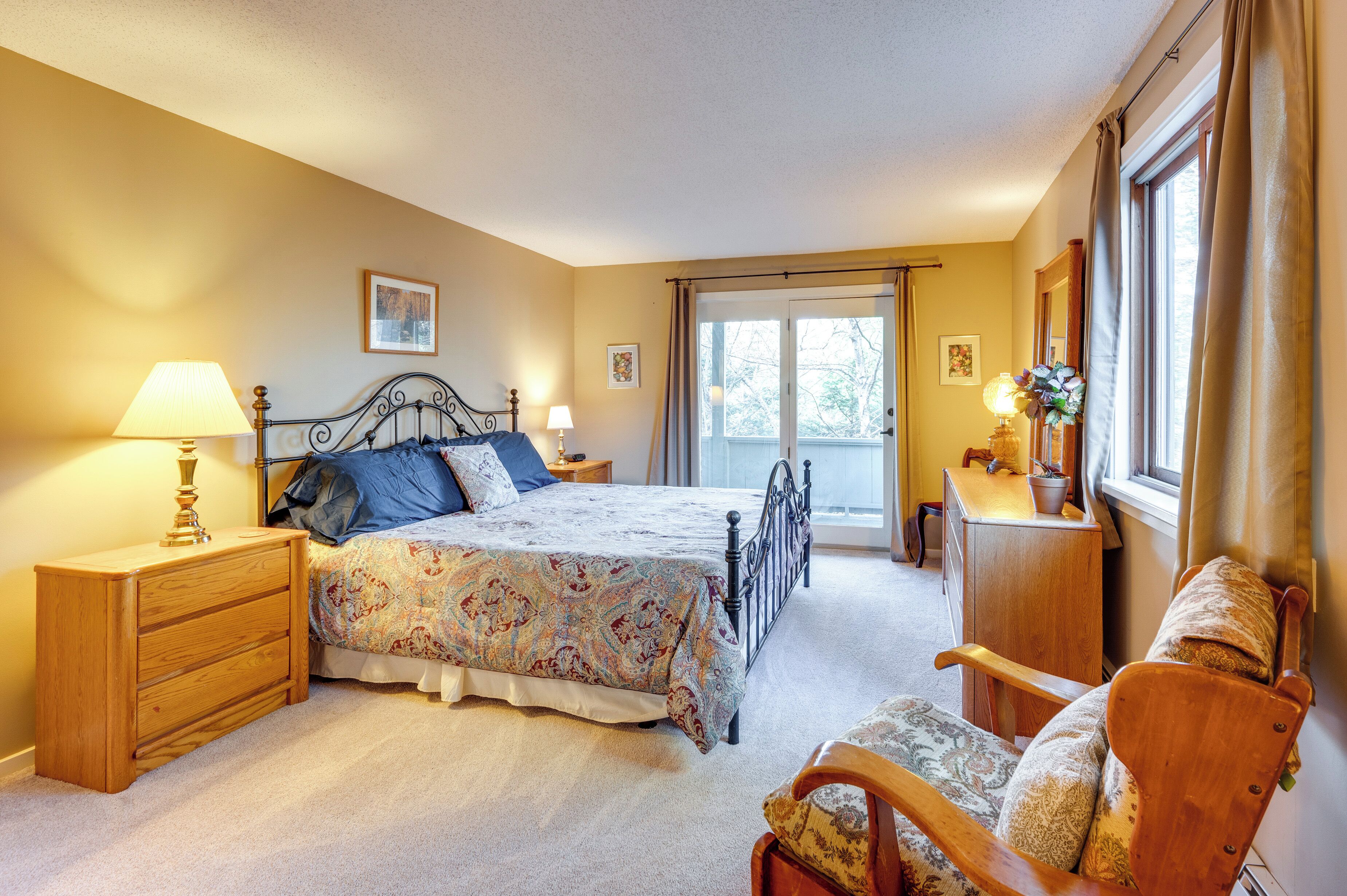 A bedroom with a bed, wooden nightstands, a chair, a desk, and a window with curtains.