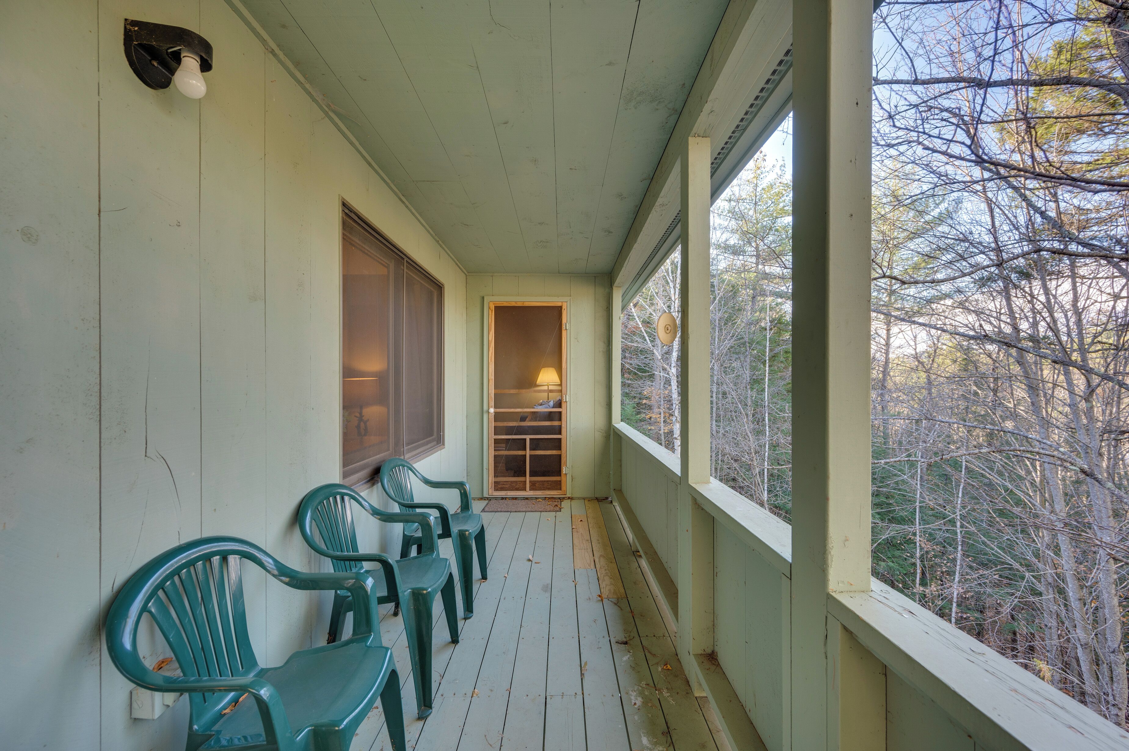 A porch with green chairs, a wooden door, and a window with a view of trees.