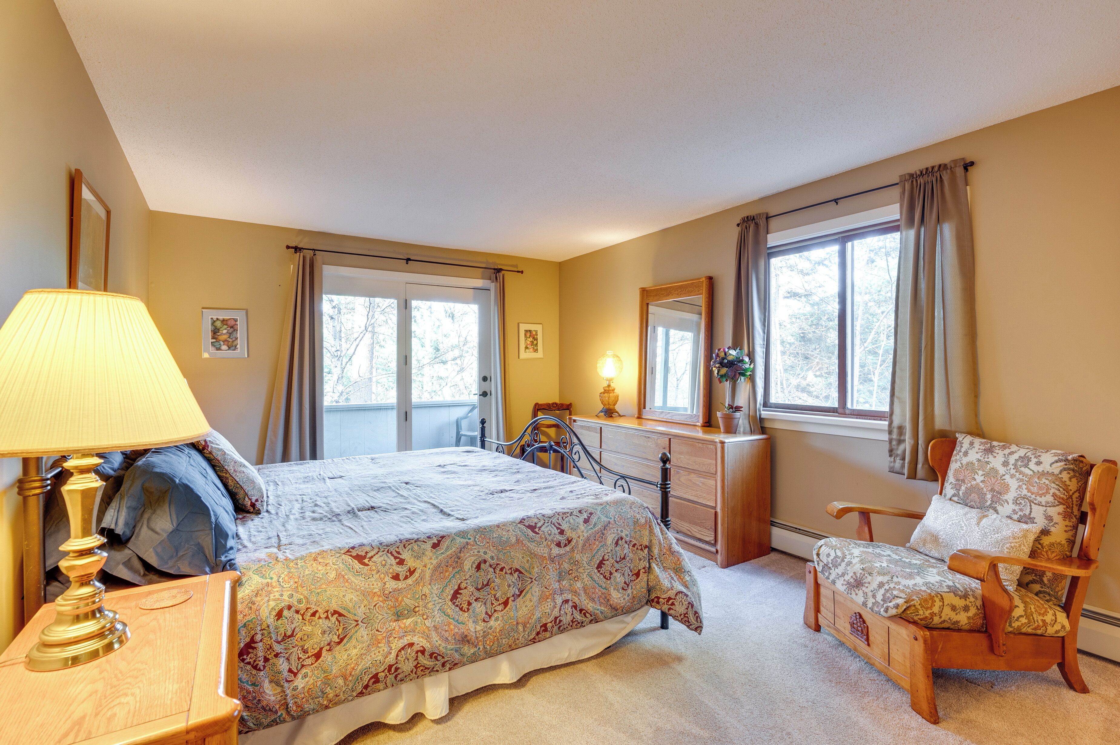 A bedroom with a bed, a chair, a dresser, a lamp, and a window with curtains.