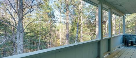 A covered porch with a view of a forest.