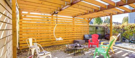 A covered patio area with wooden beams and a wooden fence. There are several chairs and a table.