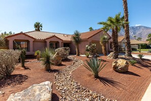 A house with a tiled roof, palm trees, and a rocky garden.
