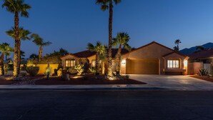 A residential house with a garage, palm trees, and a well-lit driveway at dusk. - La Buena Vida – Palm Springs Pool & Spa Retreat (Palm Springs)