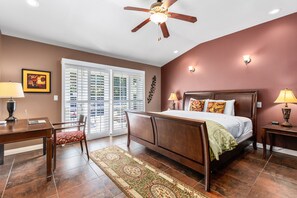 A bedroom with a bed, a desk, a chair, a ceiling fan, and a window with blinds.