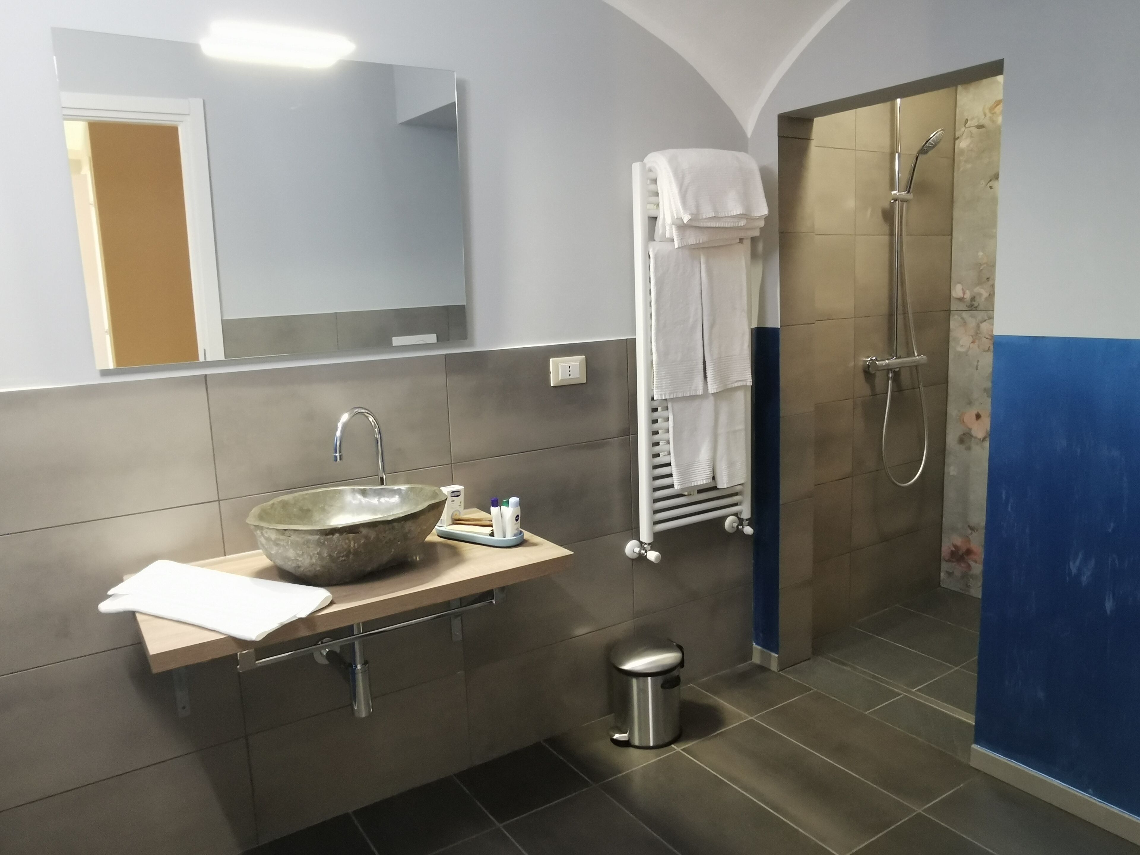 Ein Badezimmer mit einem Steinsink, einem Spiegel, einem Handtuchhalter und einer Dusche.