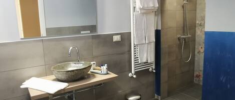 A bathroom with a stone sink, a mirror, a towel rack, and a shower.