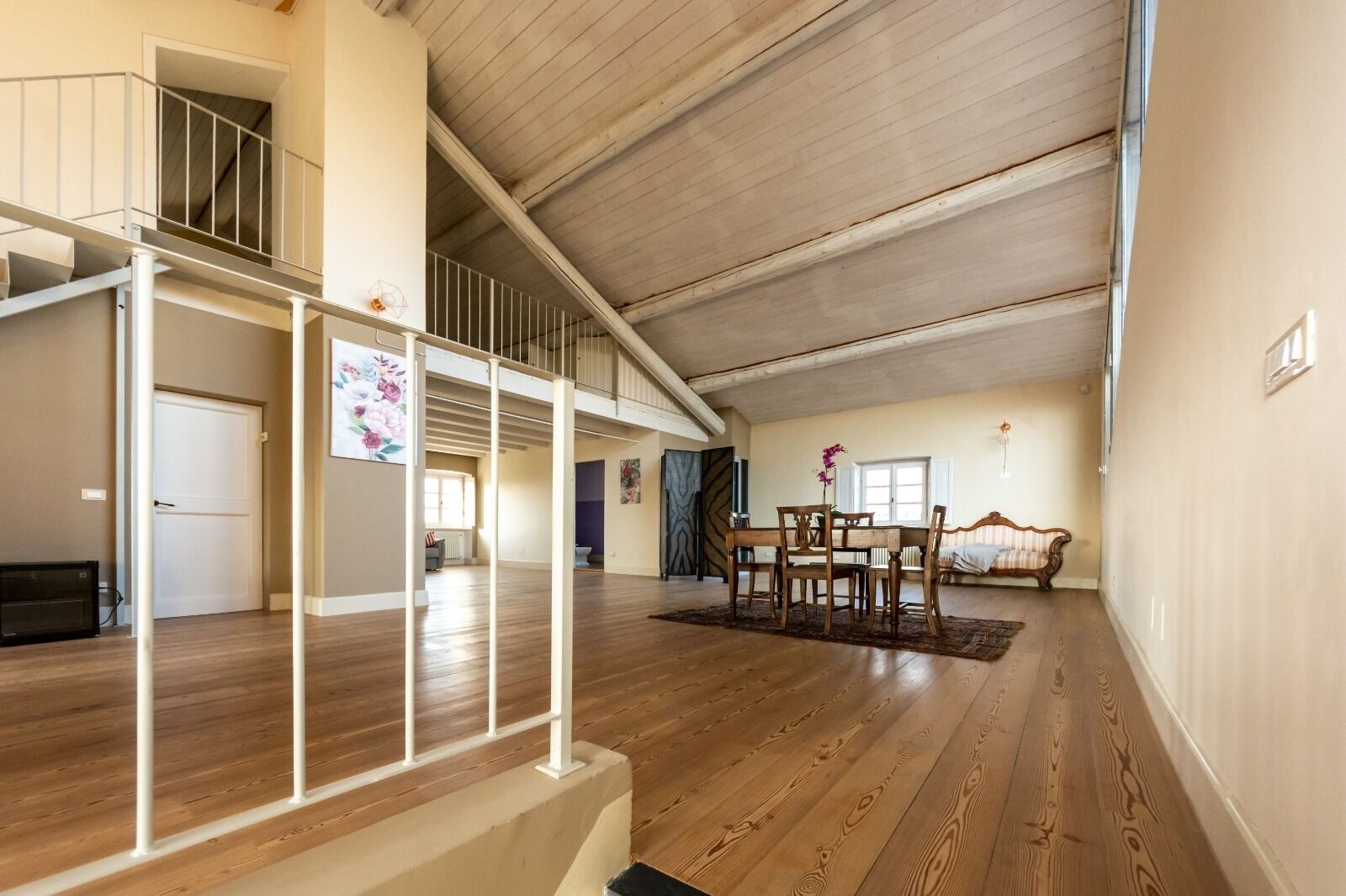 Un salón amplio con suelo de madera, una mesa de comedor con sillas, un sofá y una escalera con barandilla.