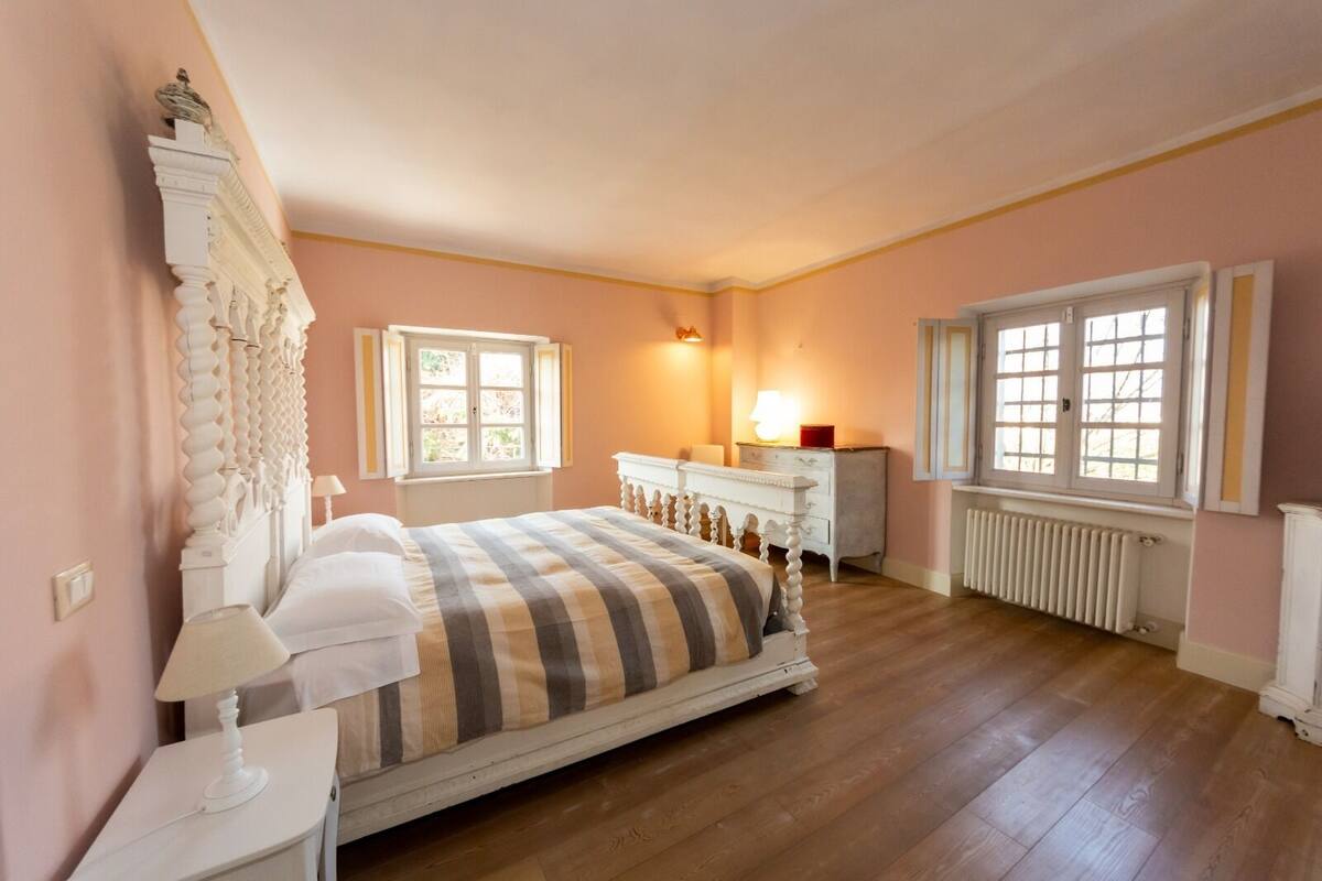 A bedroom with a large bed, a dresser, a nightstand, and two windows.