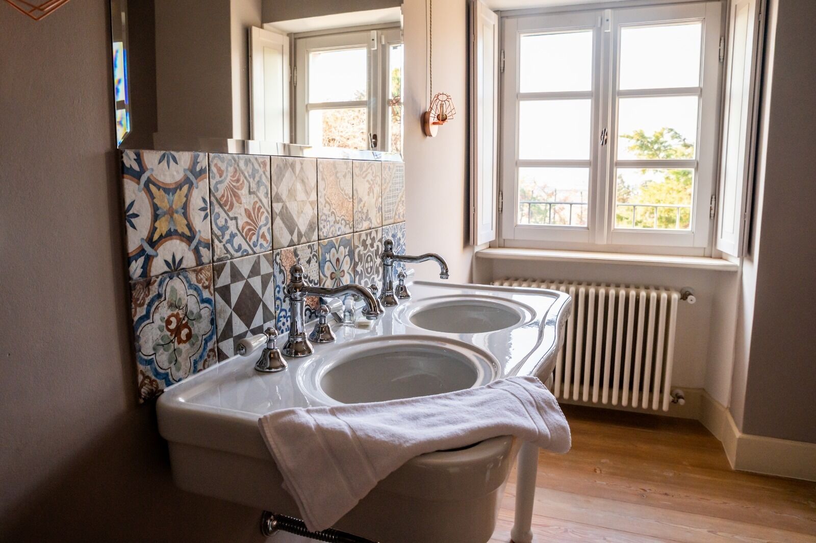 Ein Badezimmer mit zwei Waschbecken, einer Fliesenrückwand, einer Heizung und einem Fenster mit Blick.