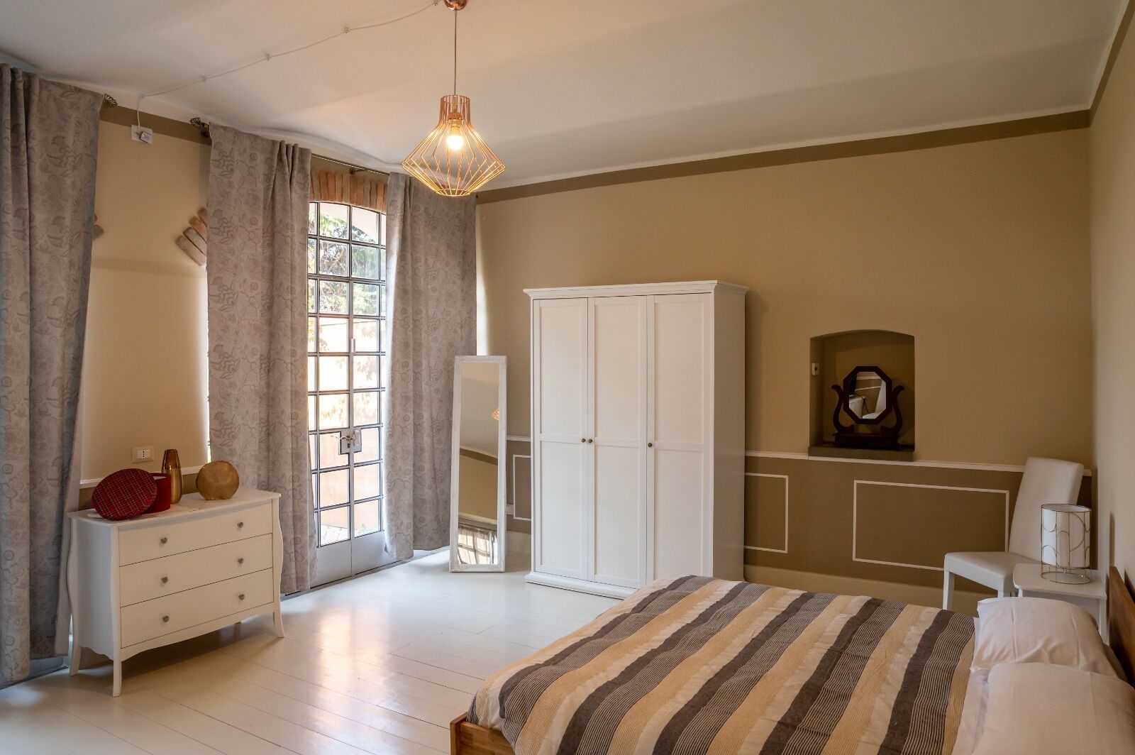 A bedroom with a bed, a wardrobe, a dresser, a mirror, and a hanging light fixture.