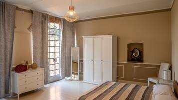 A bedroom with a bed, a wardrobe, a dresser, a mirror, and a hanging light fixture.