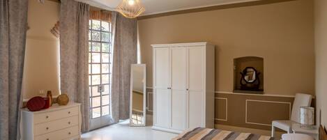 A bedroom with a bed, a wardrobe, a dresser, a mirror, and a hanging light fixture.