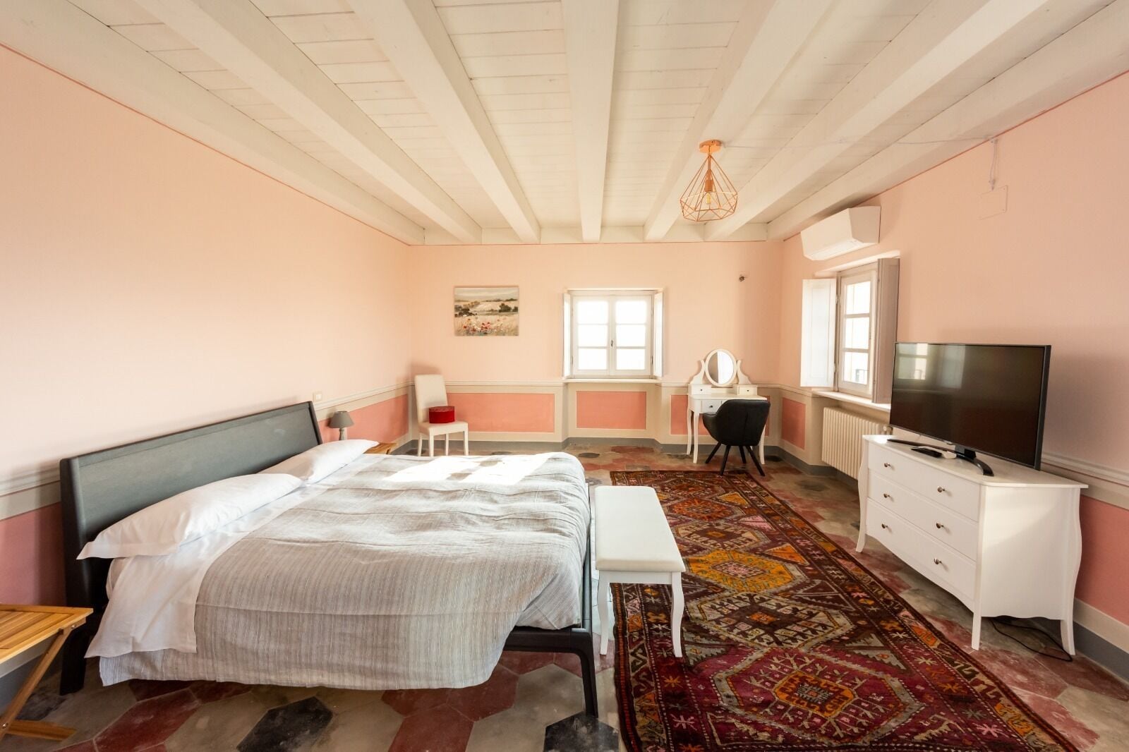 A bedroom with a bed, a desk, a chair, a television, and a patterned rug.