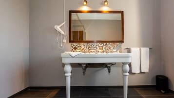 A bathroom with a white pedestal sink, a tiled backsplash, and a mirror above it. There are two white towels hanging on the wall and a hairdryer on the left.