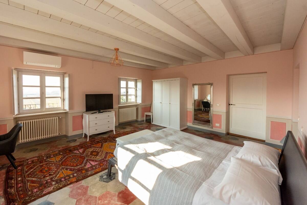 A bedroom with a large bed, a dresser, a television, and a window.