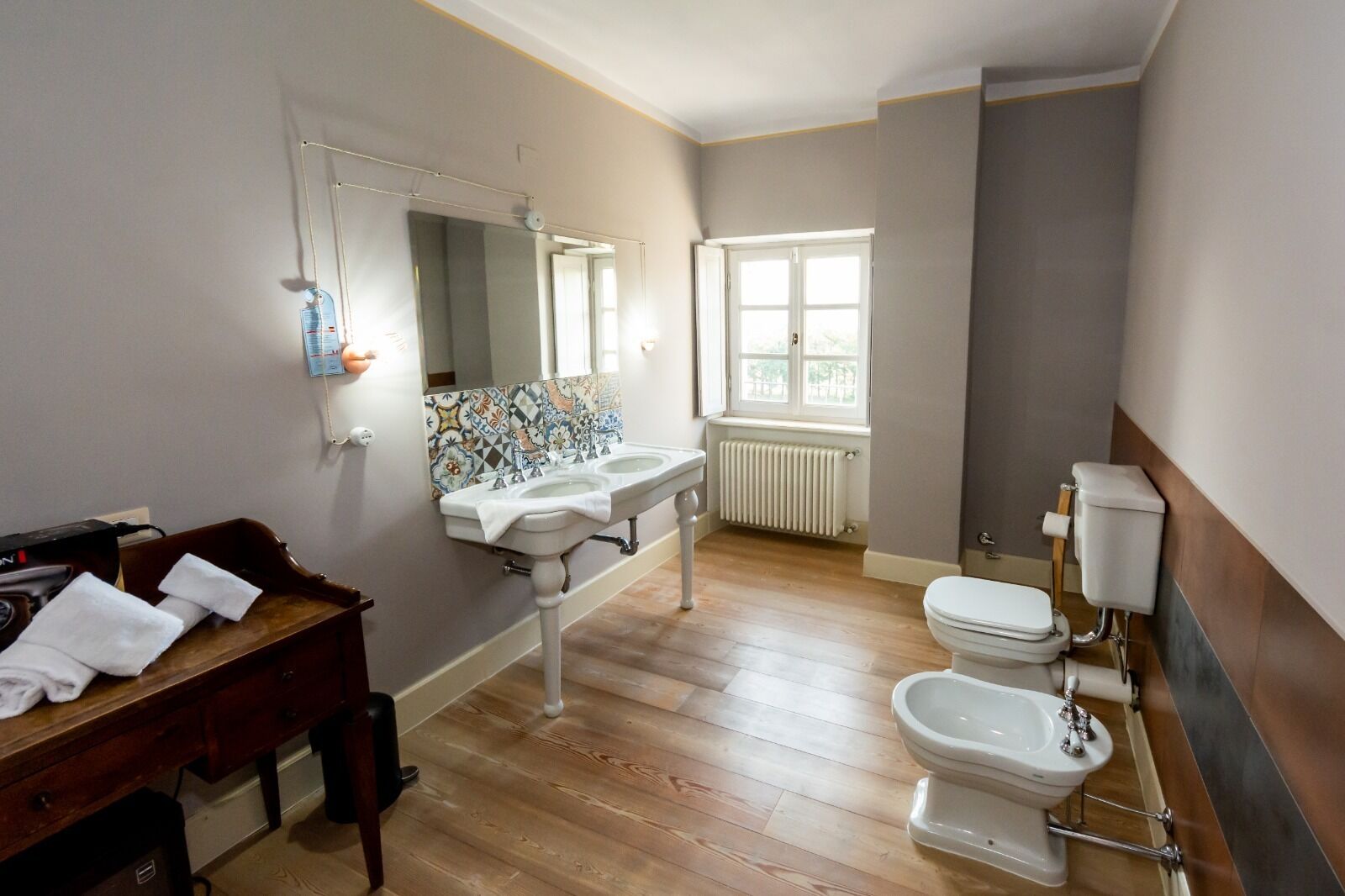 A bathroom with a wooden floor, two sinks, a toilet, and a window providing natural light.