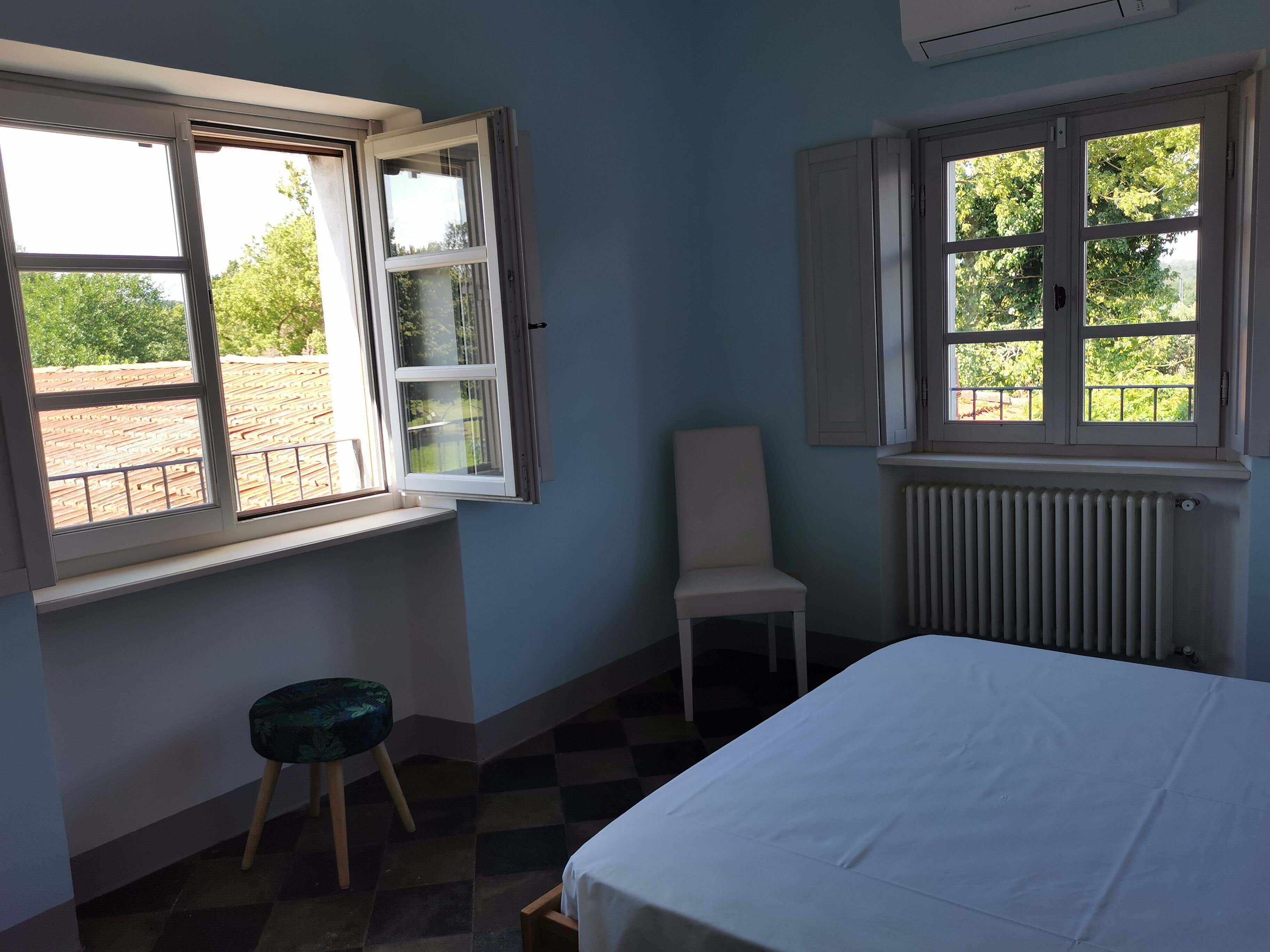 A bedroom with a bed, two windows, a radiator, and a chair.