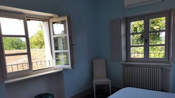 A bedroom with a bed, two windows, a radiator, and a chair.