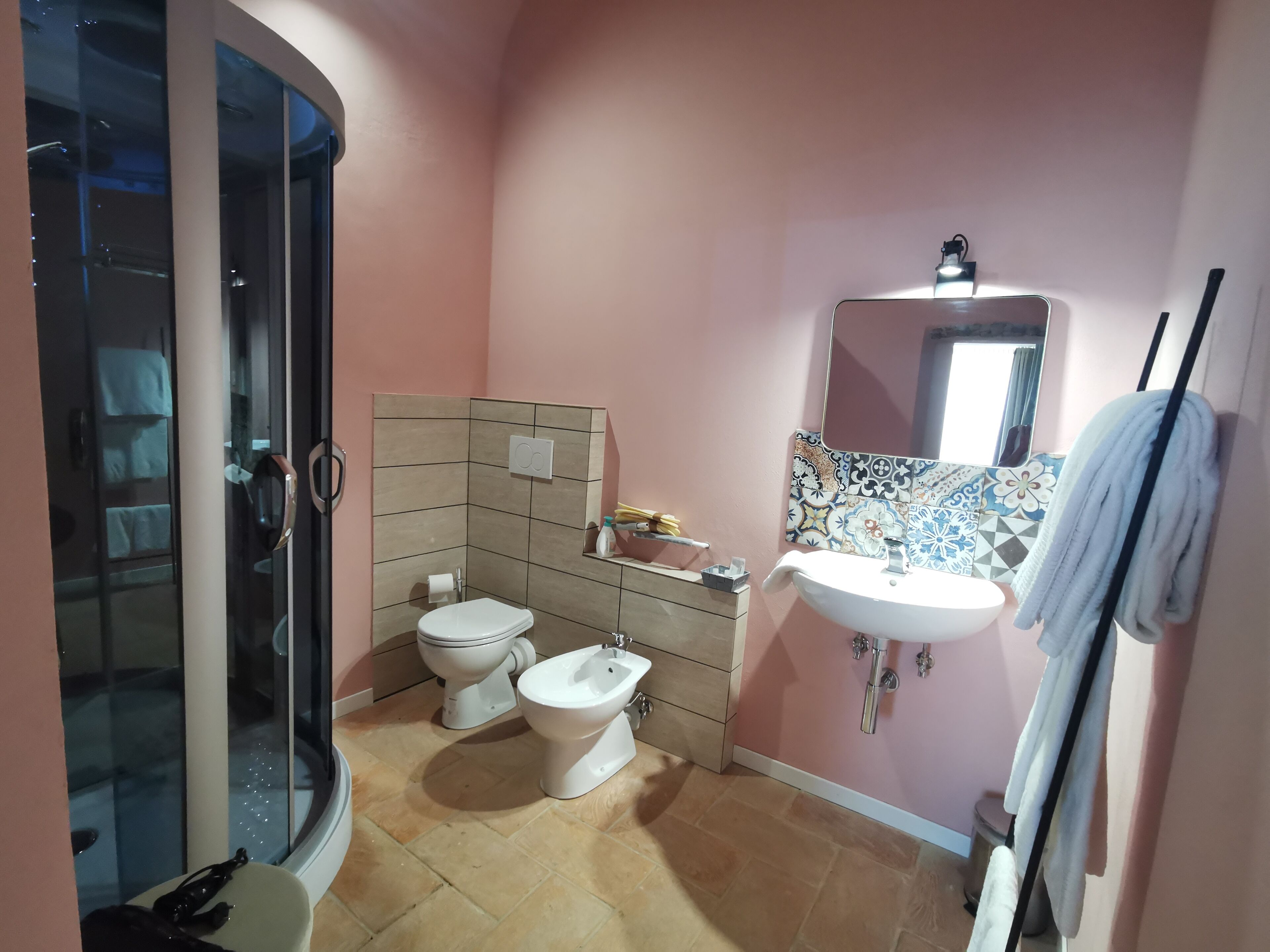 A bathroom with a glass shower enclosure, two toilets, a sink, and a mirror.
