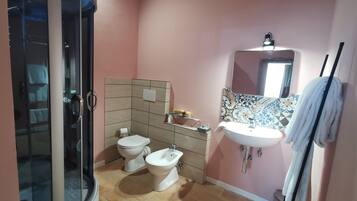 A bathroom with a glass shower enclosure, two toilets, a sink, and a mirror.