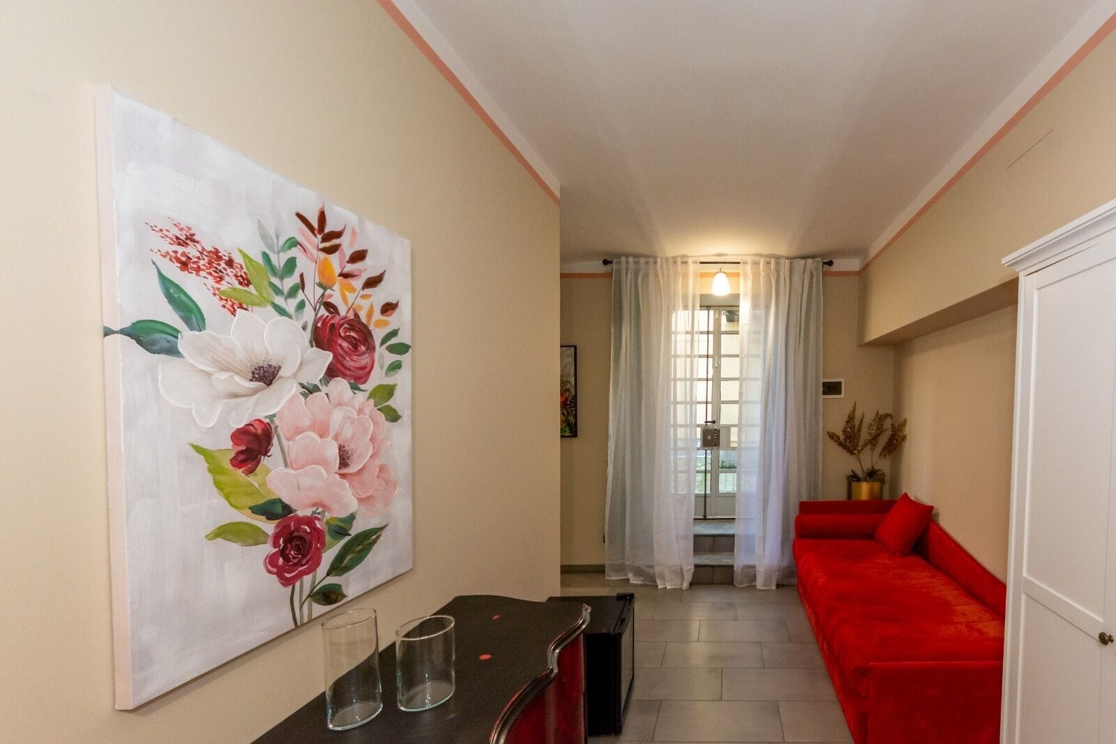 Ein Flur mit einem roten Sofa, einem Blumenbild und einem Essbereich mit Tisch und Gläsern.