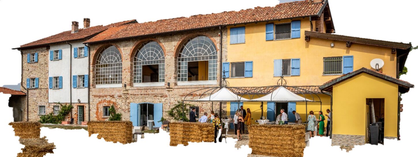 Ein traditionelles Gebäude mit Rundbogenfenstern und einer gelben Fassade, mit Außenbestuhlung und Heuballen.