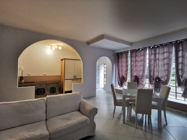 A modern living room with a sofa, dining table, and chairs. There is a kitchen area with cabinets and a fireplace. - Tenuta san Giorgio (Serravalle Scrivia)