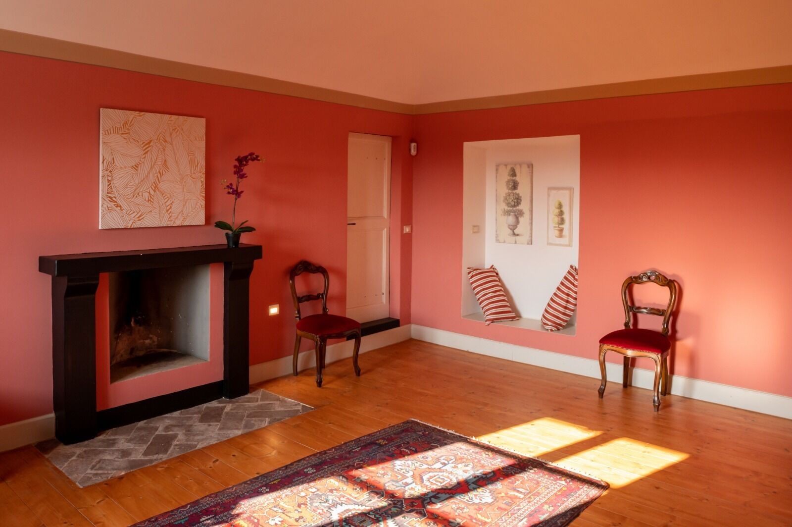 Une pièce avec une cheminée, deux fauteuils, un tapis et des œuvres d’art accrochées aux murs.