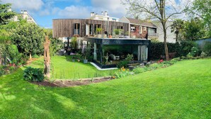 A modern house with a glass conservatory, a well-maintained garden, and a wooden deck.