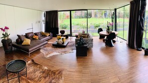 A modern living room with a curved floor, a brown leather sofa, a patterned armchair, a round coffee table, and a dining area with a table and chairs.
