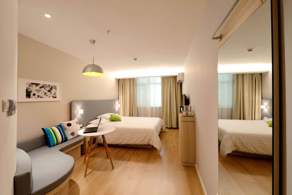 Quarto de hotel com cama, escrivaninha com laptop, sofá e espelho.