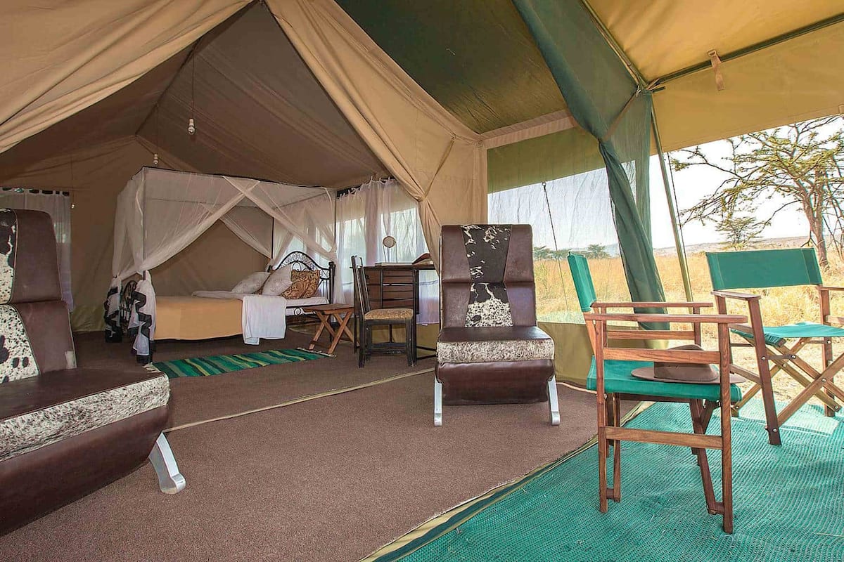 Acomodação em tenda com cama, área de estar e uma mesa.