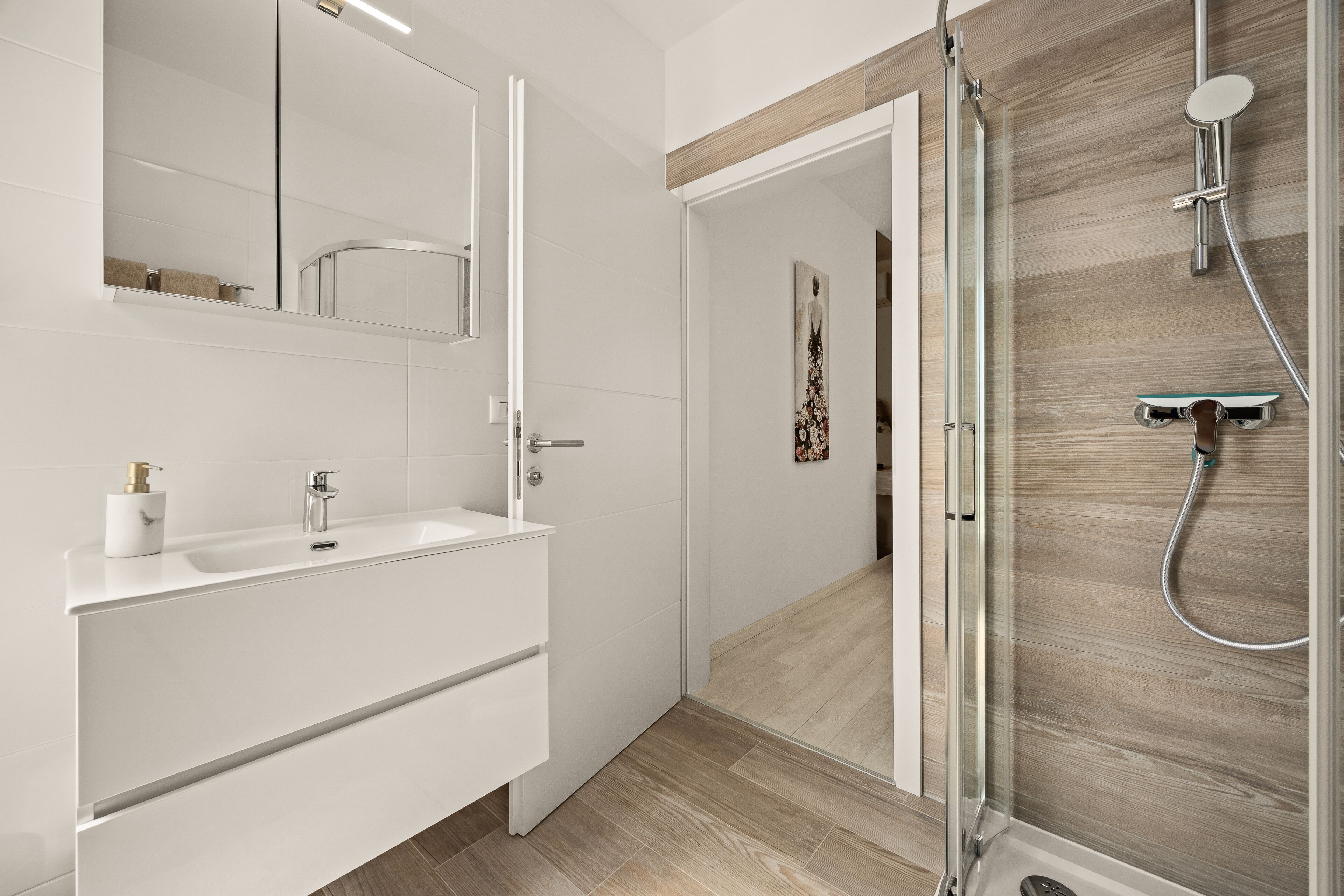 A modern bathroom with a white vanity, a glass shower enclosure, and a wooden accent wall.