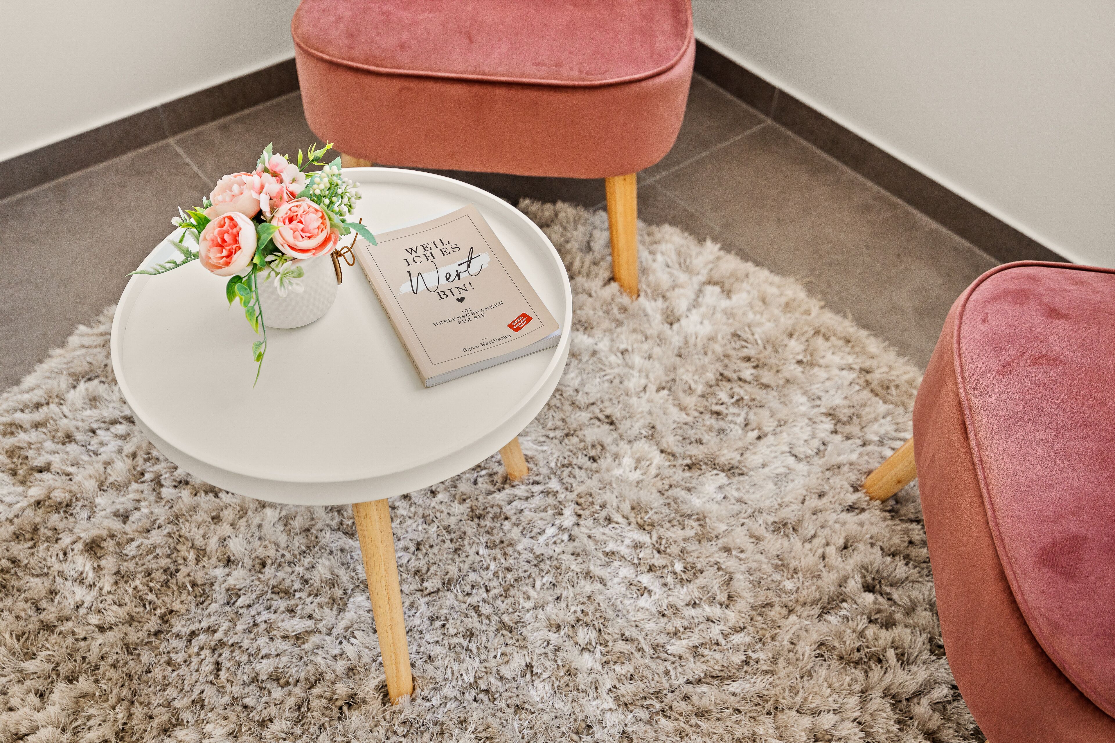 A round white table with a book and a floral arrangement on it, placed on a fluffy rug.