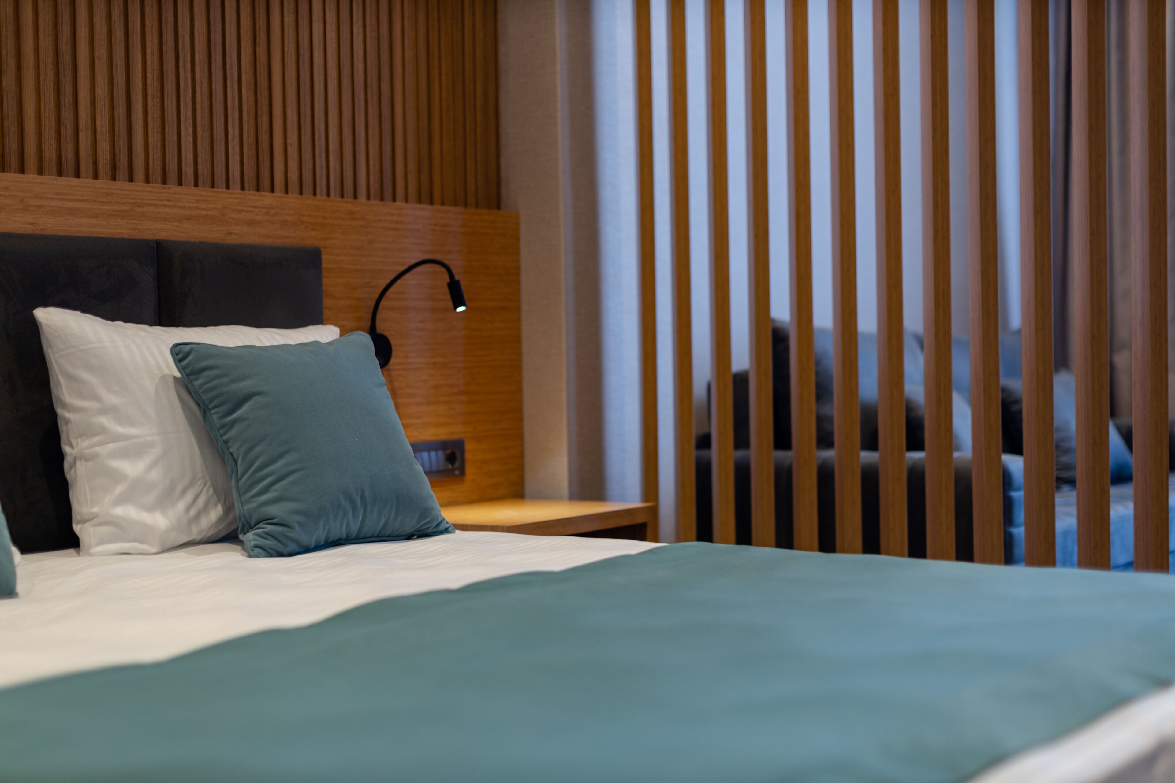 A hotel room with a bed, pillows, a nightstand, a lamp, and vertical blinds.