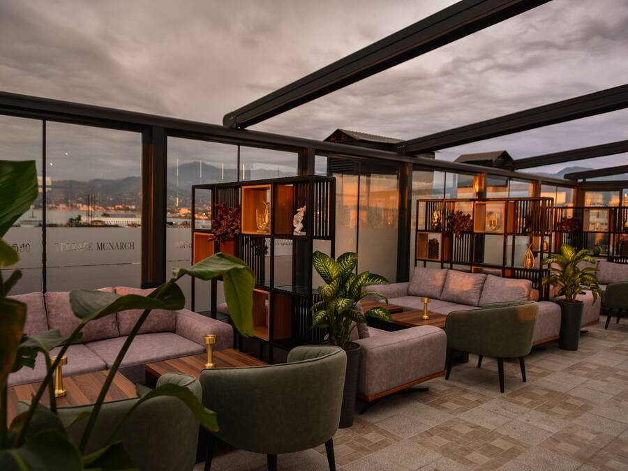 A modern lounge area with sofas and tables, large windows offering a view of a cityscape and water.