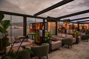 A modern lounge area with sofas and tables, large windows offering a view of a cityscape and water.