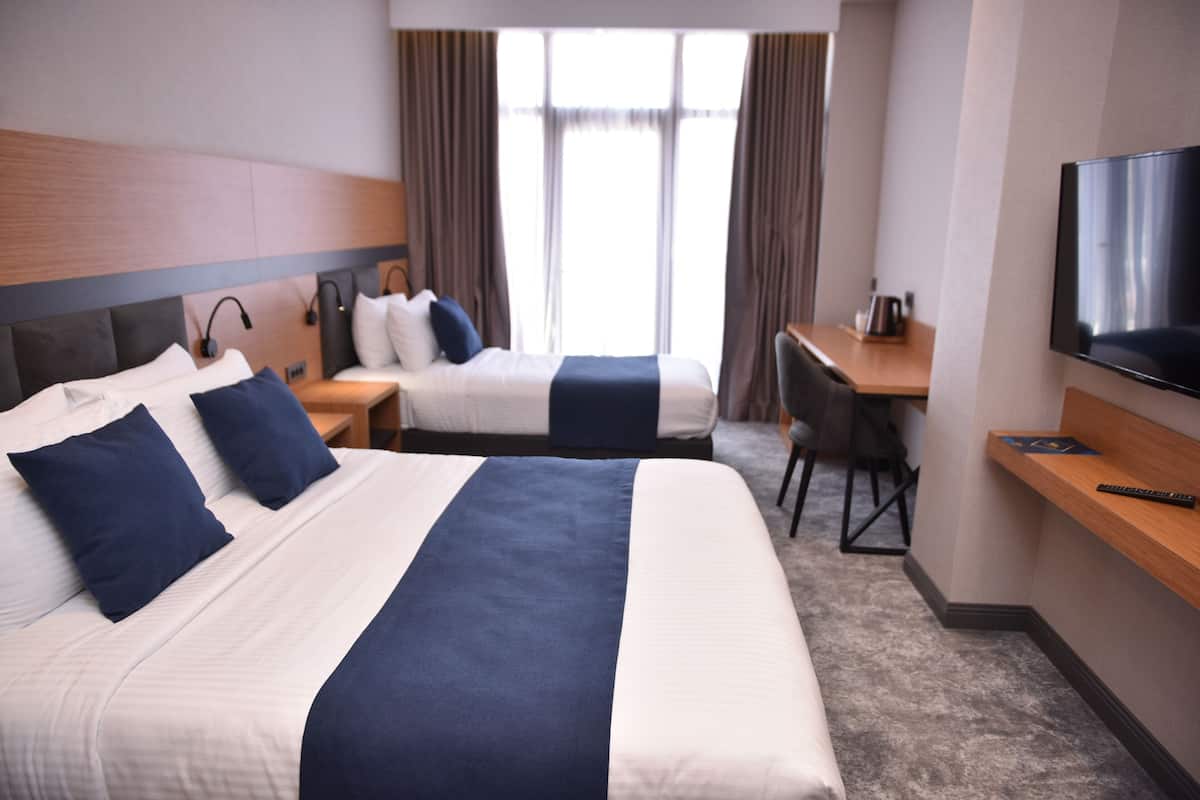 Habitación de hotel con dos camas, un escritorio, un televisor y una ventana con cortinas.