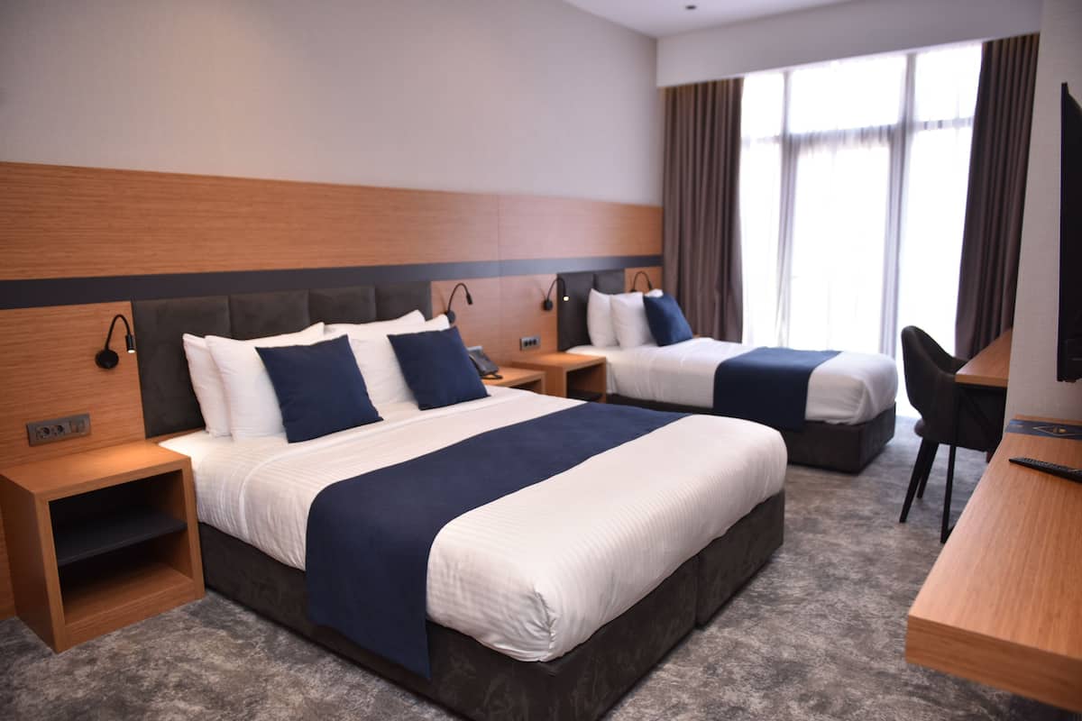 Habitación de hotel con dos camas, un escritorio y una silla. Hay mesitas de noche con lámparas y un televisor sobre el escritorio.