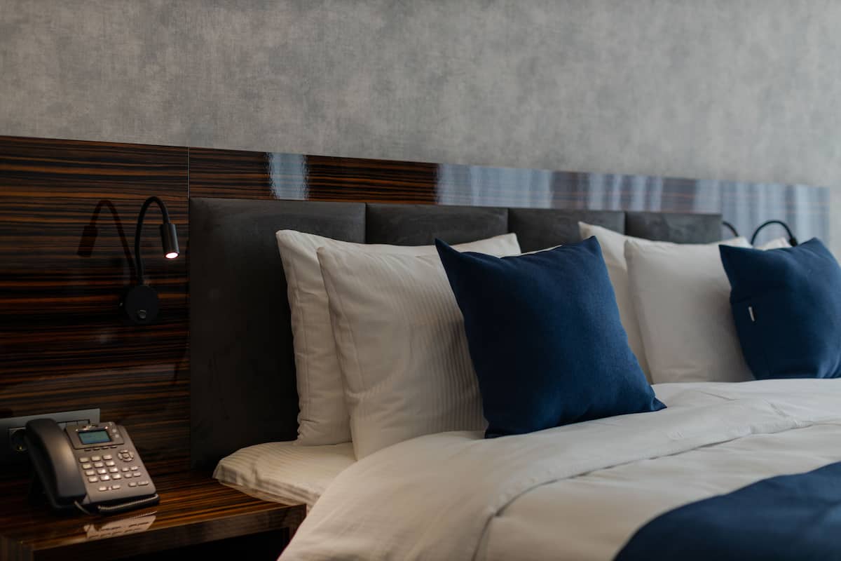 Habitación de hotel con cama, almohadas, mesita de noche con teléfono y una lámpara de pared.