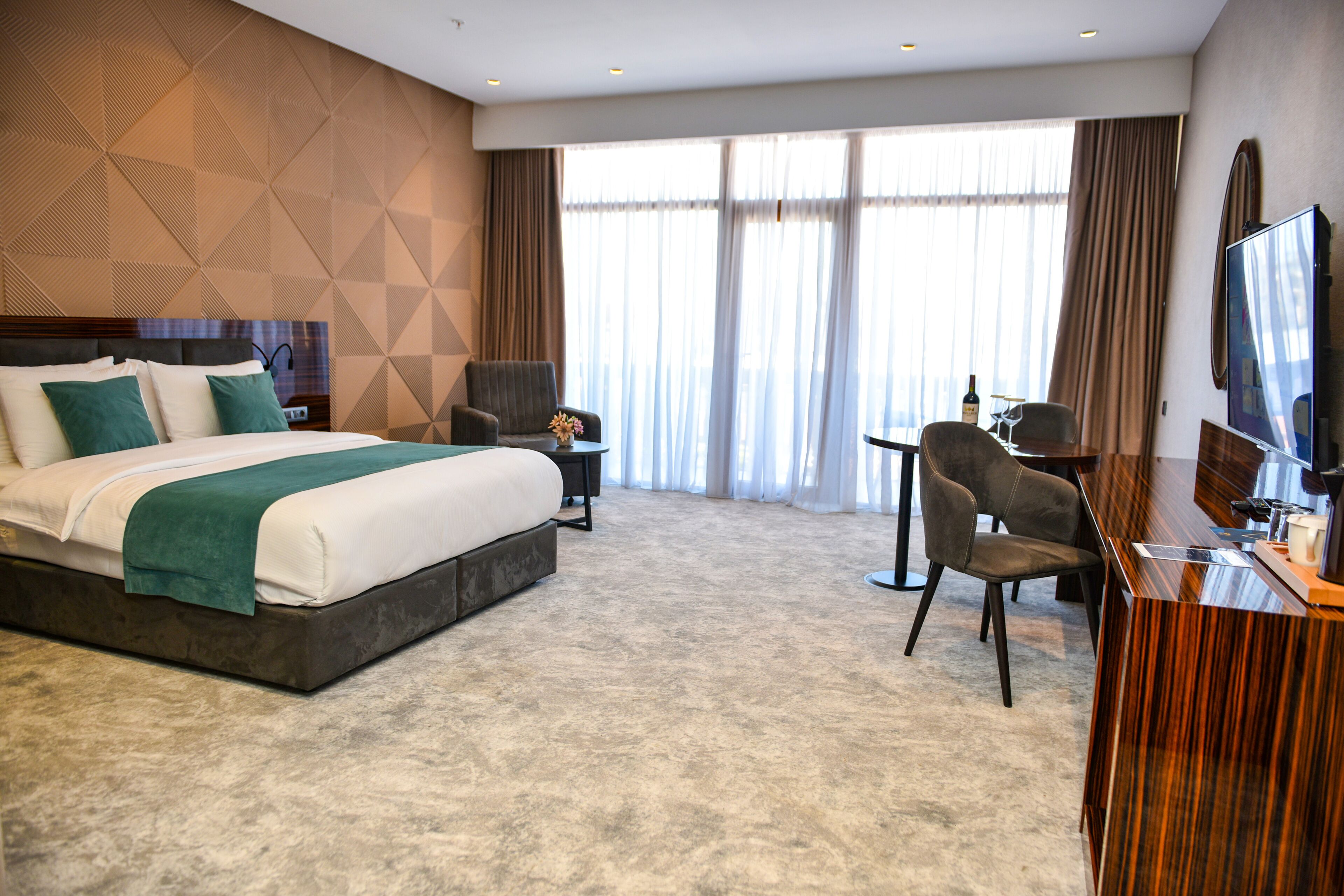 A hotel room with a large bed, a desk with a chair, a TV, and a window with curtains.