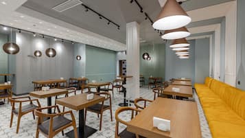 A modern cafe with wooden tables and chairs, a yellow sofa, and pendant lighting.