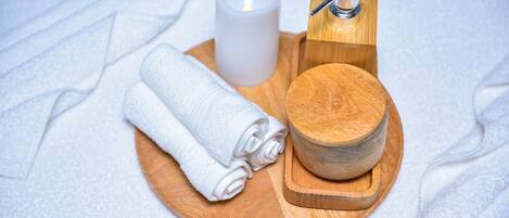 A wooden tray with a rolled white towel, a candle, and a wooden container.