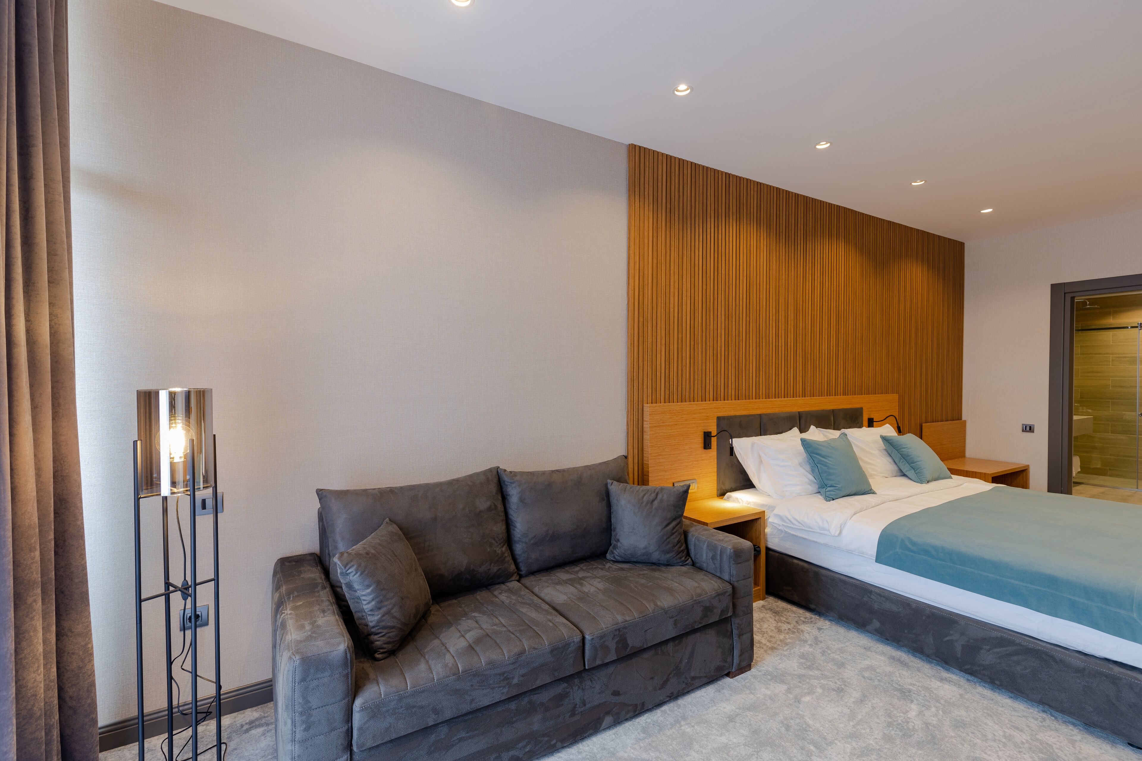 A modern bedroom with a large bed, a grey sofa, and a floor lamp.