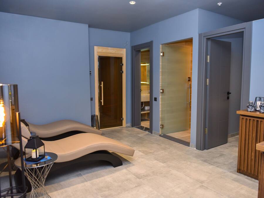 A modern spa room with a massage table, a small side table with a candle, and a cabinet with decorative items.