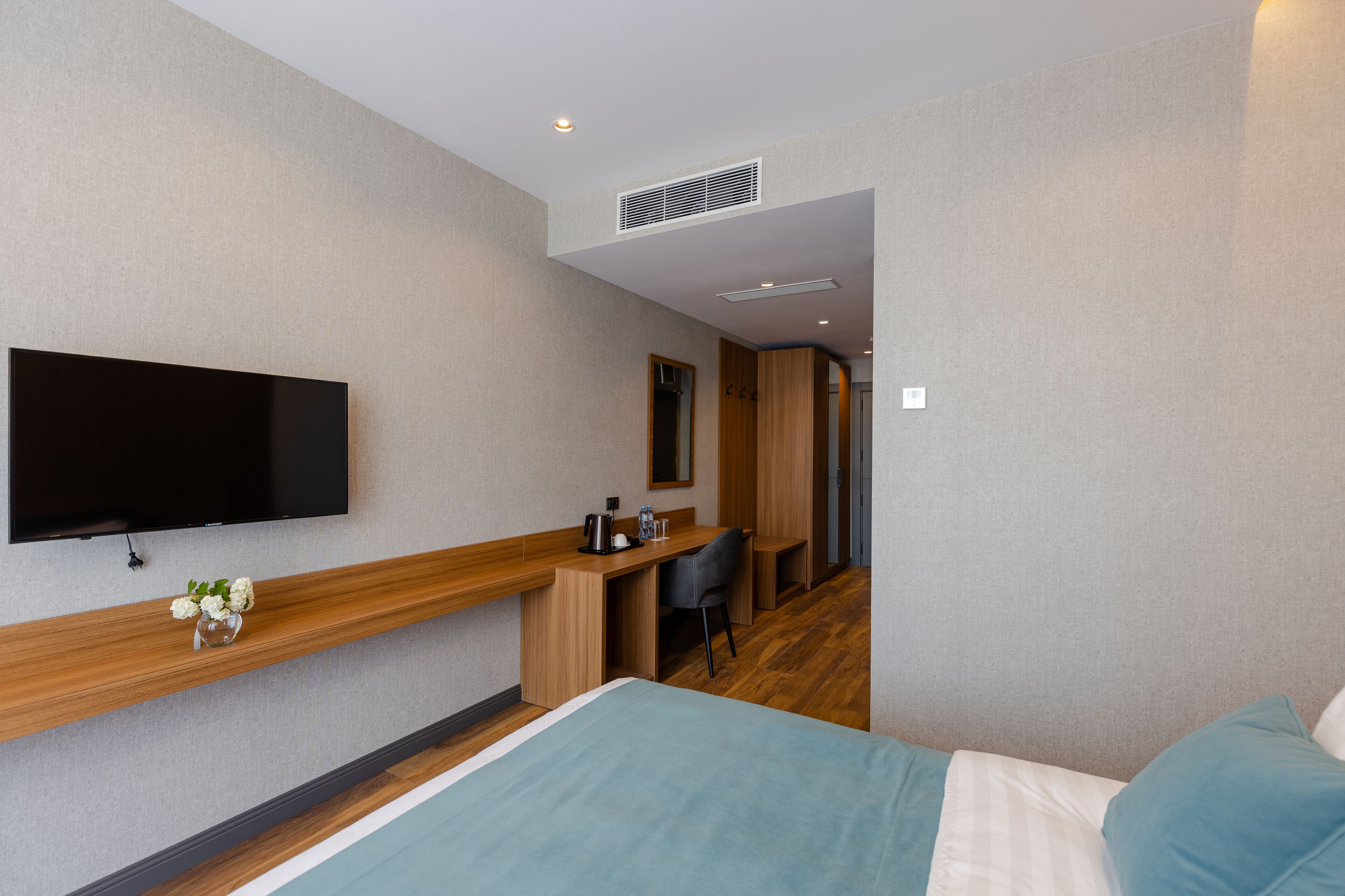 Une chambre d’hôtel comprenant un lit, un bureau avec une chaise, un téléviseur à écran plat fixé au mur et un petit vase avec des fleurs posé sur le bureau.