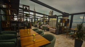 Un saló modern amb una taula de fusta, cadires tapissades de verd i vista a un skyline urbà.