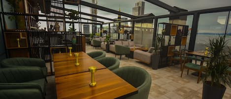 Un salón moderno con una mesa de madera, sillas tapizadas en verde y vistas a un horizonte urbano.