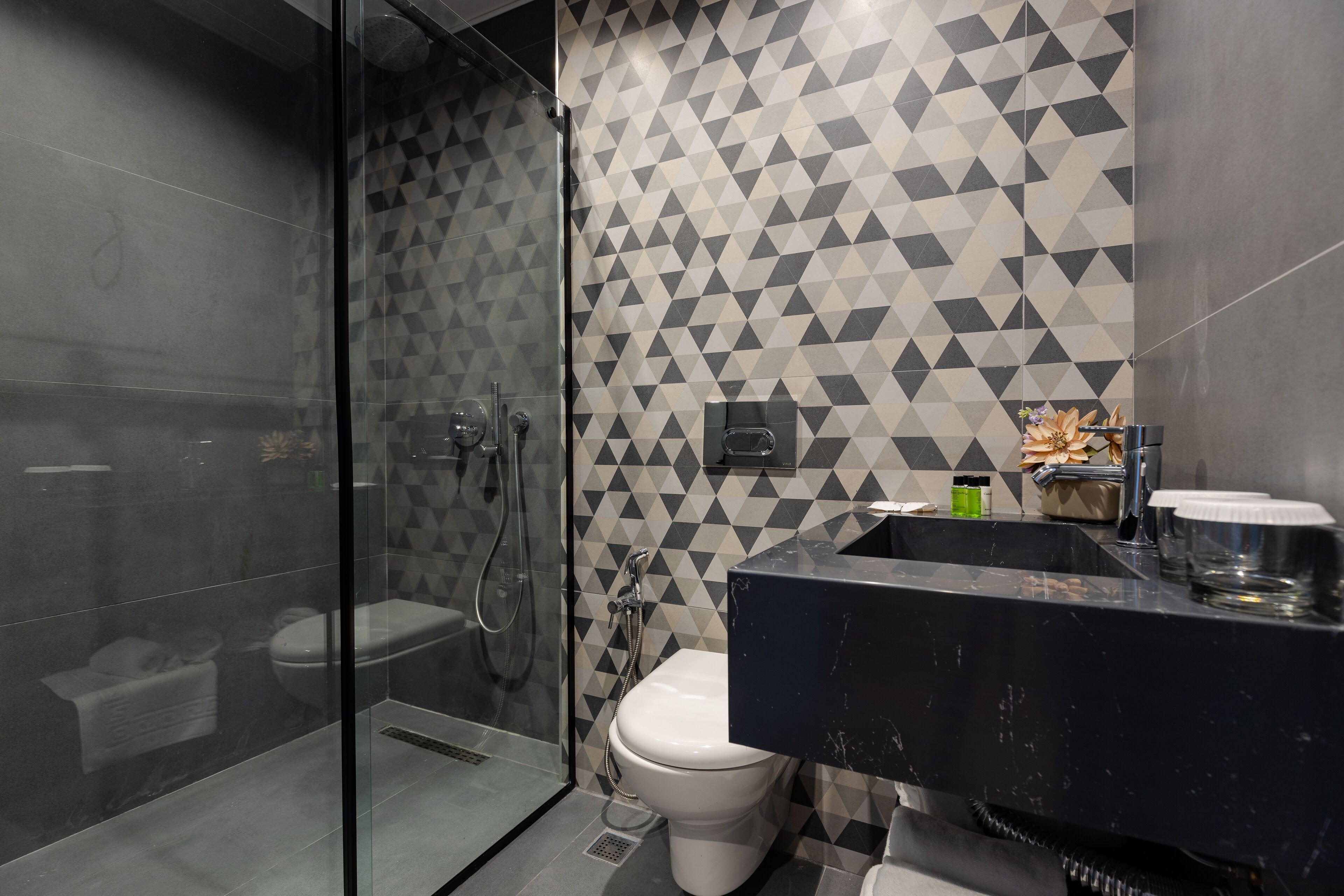 Un baño moderno con un salpicadero de azulejos geométricos, ducha con cerramiento de vidrio y lavamanos de mármol negro.