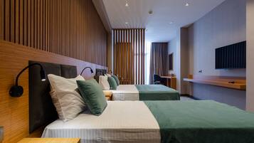 Habitación de hotel con dos camas, paneles de madera en la pared, un televisor de pantalla plana y un escritorio con una silla.